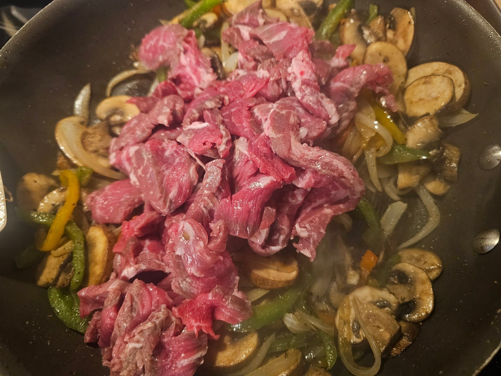Thinly sliced sirloin cooking with peppers, onions, and mushrooms